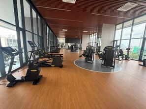 Een sportschool met cardioapparatuur, gewichten en grote ramen met uitzicht over de stad.