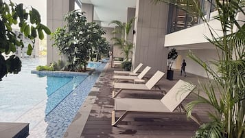 Una piscina interior con suelo de baldosas, sillones de descanso y plantas en macetas.
