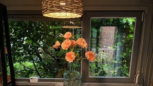 Ein Holzespeisetisch mit Stühlen, eine Vase mit Blumen, eine Pendelleuchte und ein Fenster mit Blick auf Grünflächen.