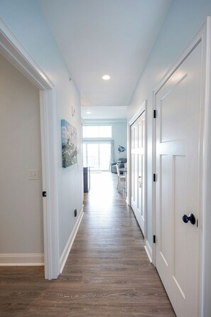 A hallway with wooden flooring, white walls, and doors on both sides. - Breezy Beach Haven - 3rd story 1 bedroom condo w ac, laundry, deck, elevator. (Hampton)