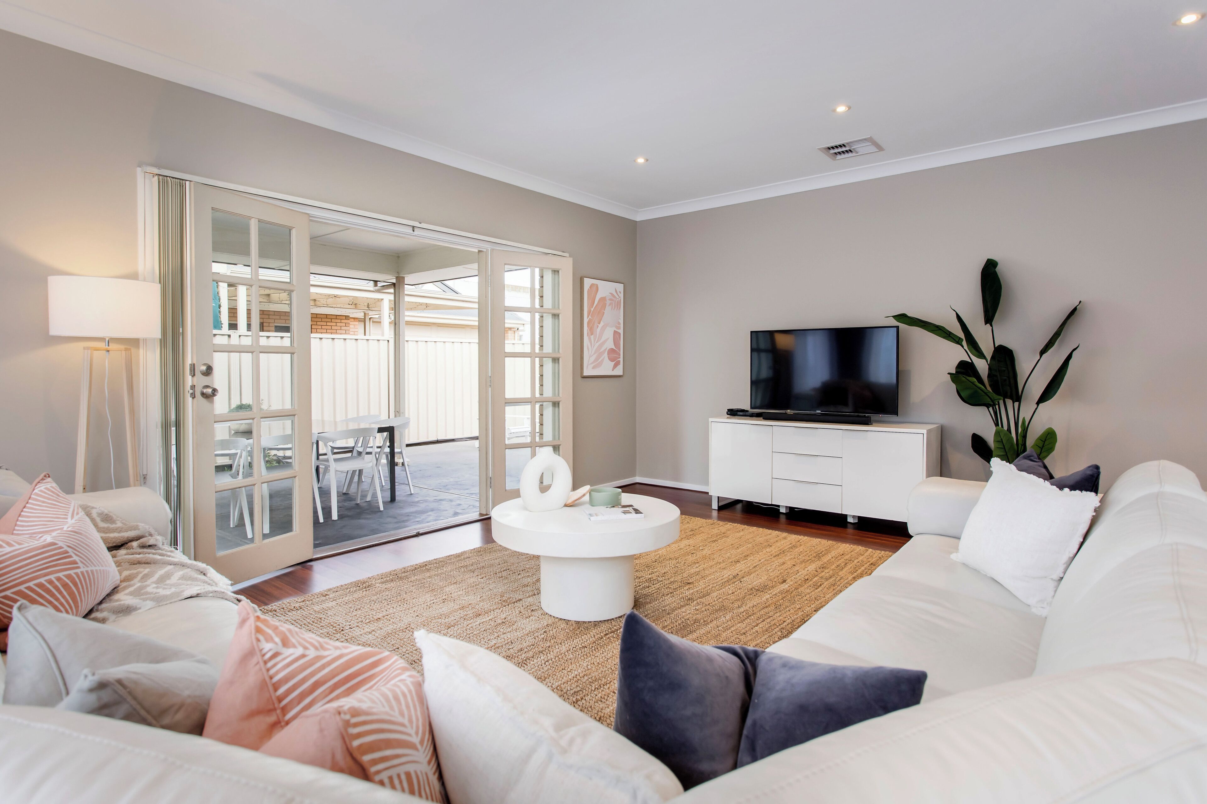 A living room with a white sofa, a coffee table, a TV, and a sliding glass door leading to an outdoor area.