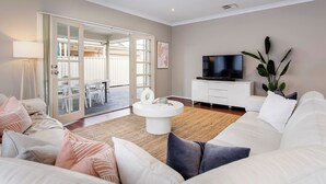 Una sala de estar con un sofá blanco, una mesa de centro, un televisor y un ventanal corredero que da a un espacio exterior.