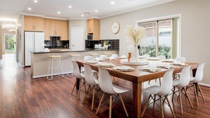 Cocina moderna con armarios de madera, una isla central y una zona de comedor con mesa de madera preparada para seis comensales.