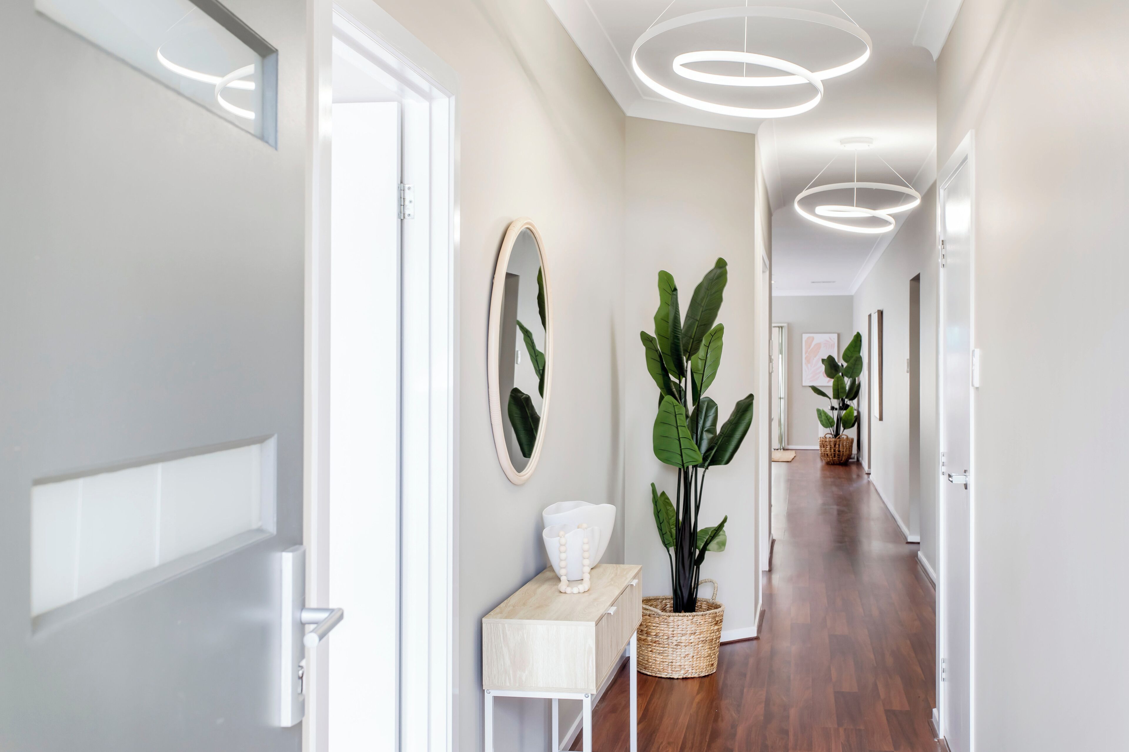 A modern hallway with a wooden floor, white walls, and a ceiling with circular light fixtures.
