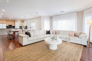 A modern living room with a sectional sofa, a coffee table, and a dining area with chairs. - Lumina A Spacious Haven Close to Adelaides Best (Allenby Gardens)