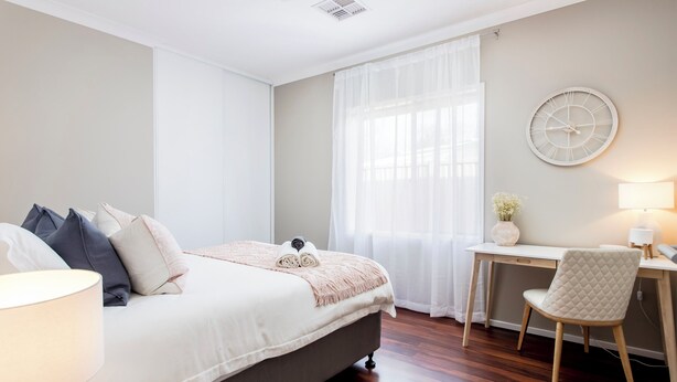 Un dormitorio con cama, mesita de noche, lámpara, silla, escritorio y un reloj en la pared.
