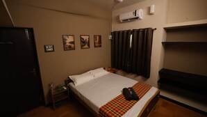 Una habitación de hotel con una cama, una mesita de noche, un aire acondicionado instalado en la pared y un juego de cortinas.