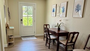 Un comedor con una mesa y sillas de madera, una puerta con ventanal y cuadros en la pared.