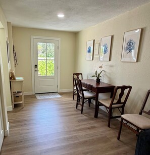 A dining area with a wooden table and chairs, a door with a window, and framed artwork on the wall. - Renovated Coastal Retreat- Walk to water, includes bikes, Bike to Pinellas Trail (Palm Harbor)