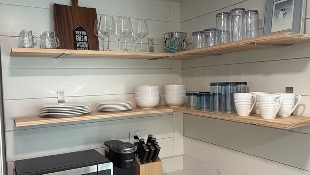 Cocina con microondas, cafetera y diferentes platos y vasos en estantes.