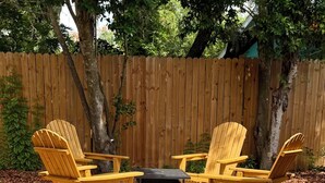 Un conjunto de sillones Adirondack de madera con una mesa y un brasero en un patio trasero.