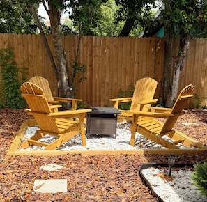 A wooden Adirondack chair set with a table and a fire pit in a backyard. - Renovated Coastal Retreat- Walk to water, includes bikes, Bike to Pinellas Trail (Palm Harbor)