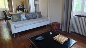 Ett vardagsrum med en soffa, ett soffbord i glas, ett schackspel och en röd pall.