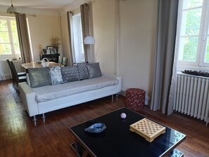 A living room with a sofa, a glass coffee table, a chess set, and a red ottoman. - 2-Bedroom Country House in the Heart of Quercy-Périgord (Gourdon)