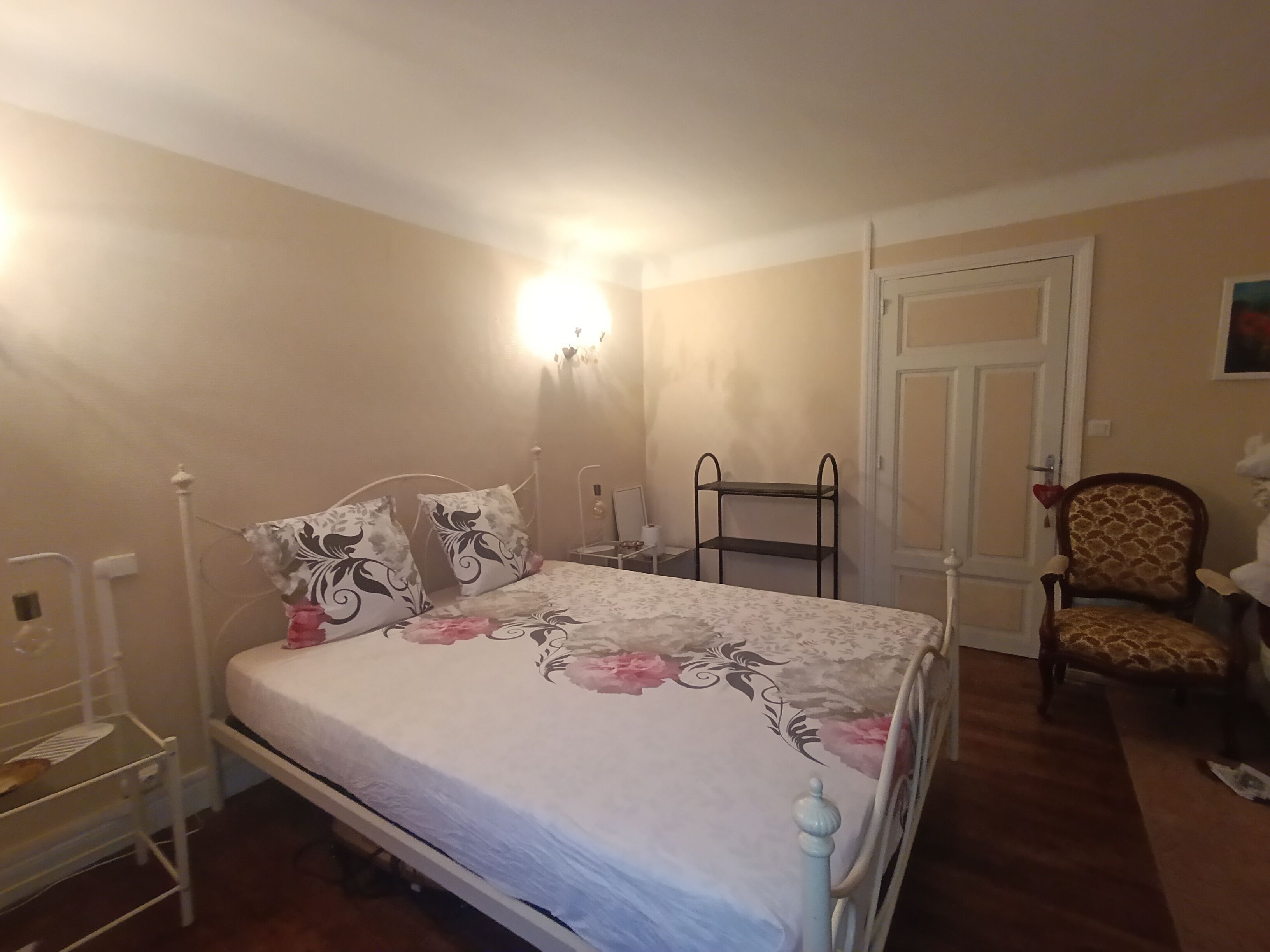 A bedroom with a bed, a chair, a shelf, and a door.