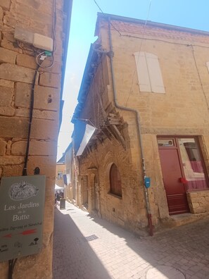 A narrow street with stone buildings, a sign for 'Les Jardins de la Butte,' and a red door on the right. - 2-Bedroom Country House in the Heart of Quercy-Périgord (Gourdon)