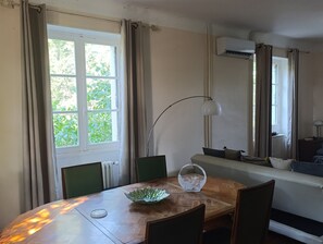A dining area with a round table, chairs, a bowl, a lamp, and a window with curtains. - 2-Bedroom Country House in the Heart of Quercy-Périgord (Gourdon)