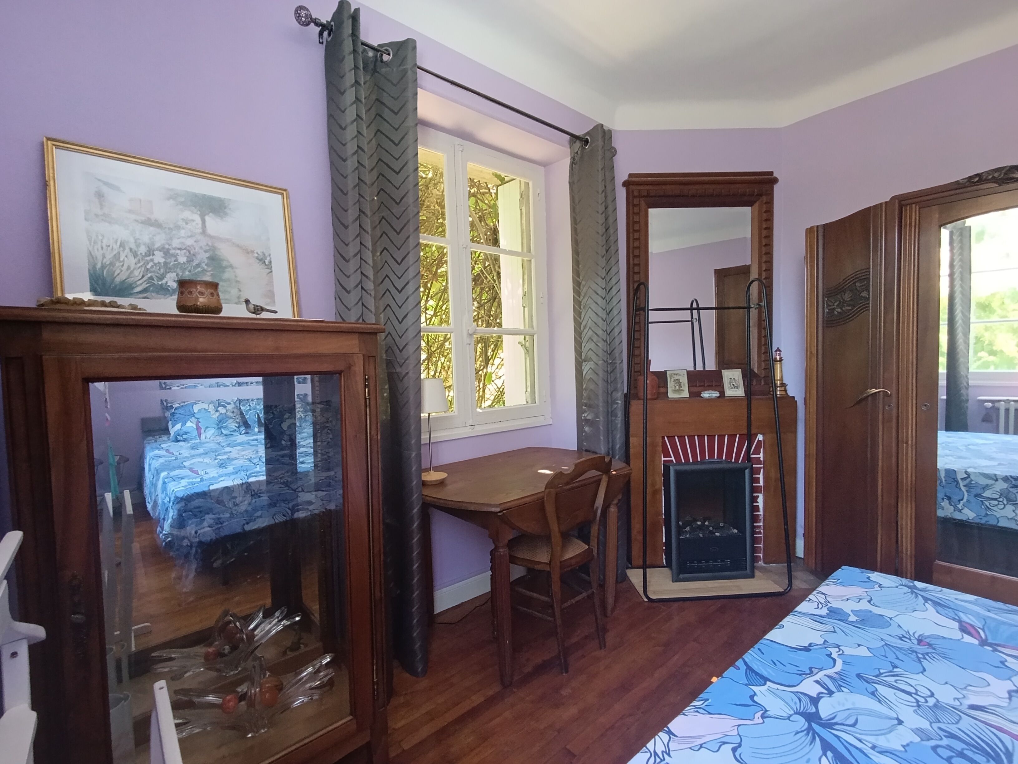 Ein Zimmer mit einem Bett, einem Schreibtisch, einem Stuhl, einem Kamin und einem fensterbehangenen Fenster.