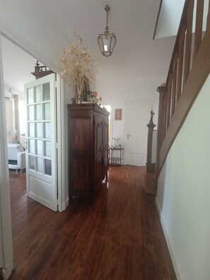 A hallway with wooden flooring, a white door, a wooden cabinet with a vase of flowers, and a hanging light fixture. - 2-Bedroom Country House in the Heart of Quercy-Périgord (Gourdon)