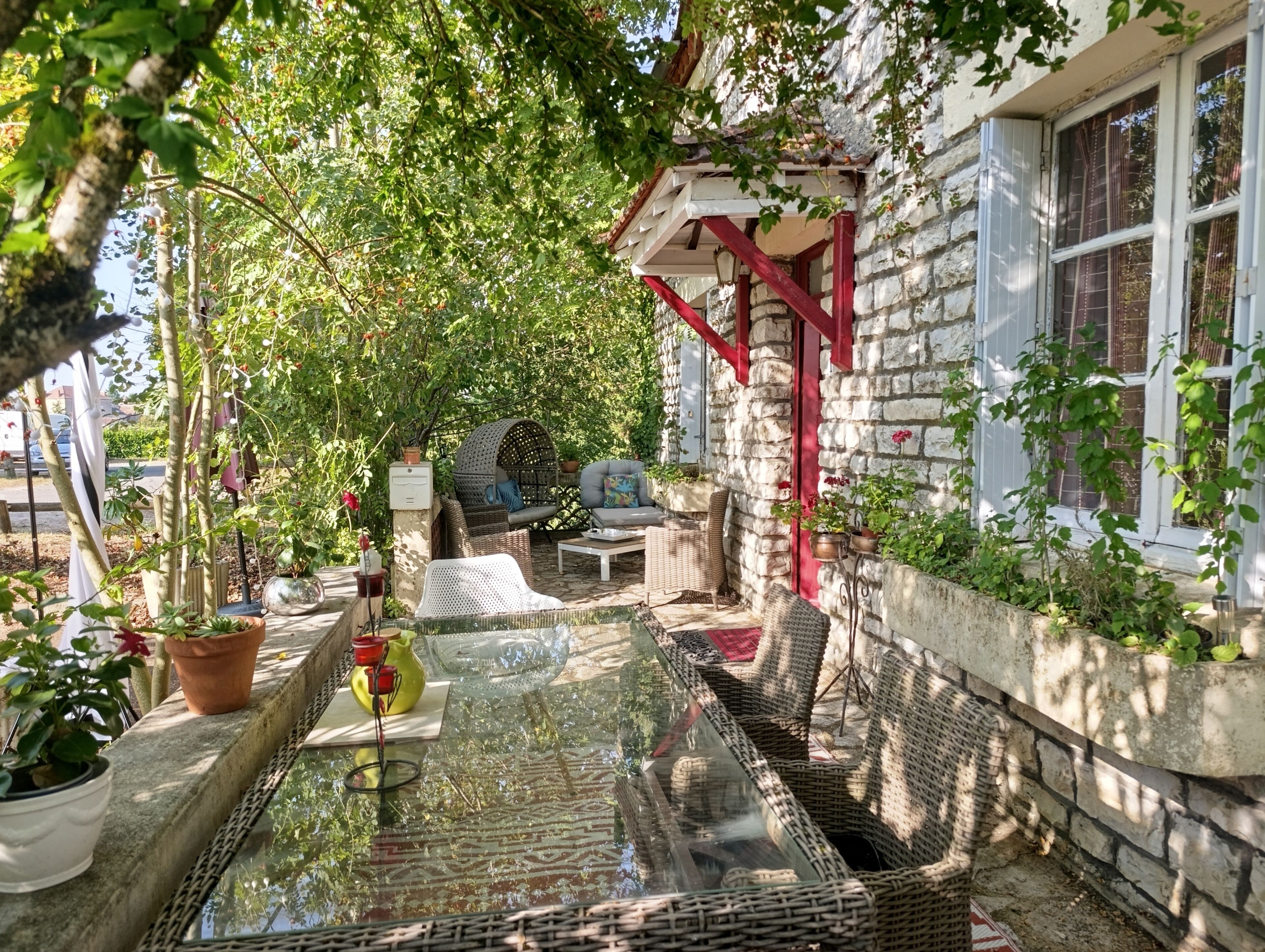 A sunlit outdoor seating area with wicker furniture, a glass table, and potted plants.