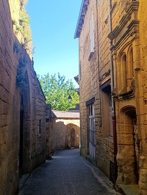 A narrow cobblestone alleyway between stone buildings with arched doorways and a clear blue sky above. - 2-Bedroom Country House in the Heart of Quercy-Périgord (Gourdon)
