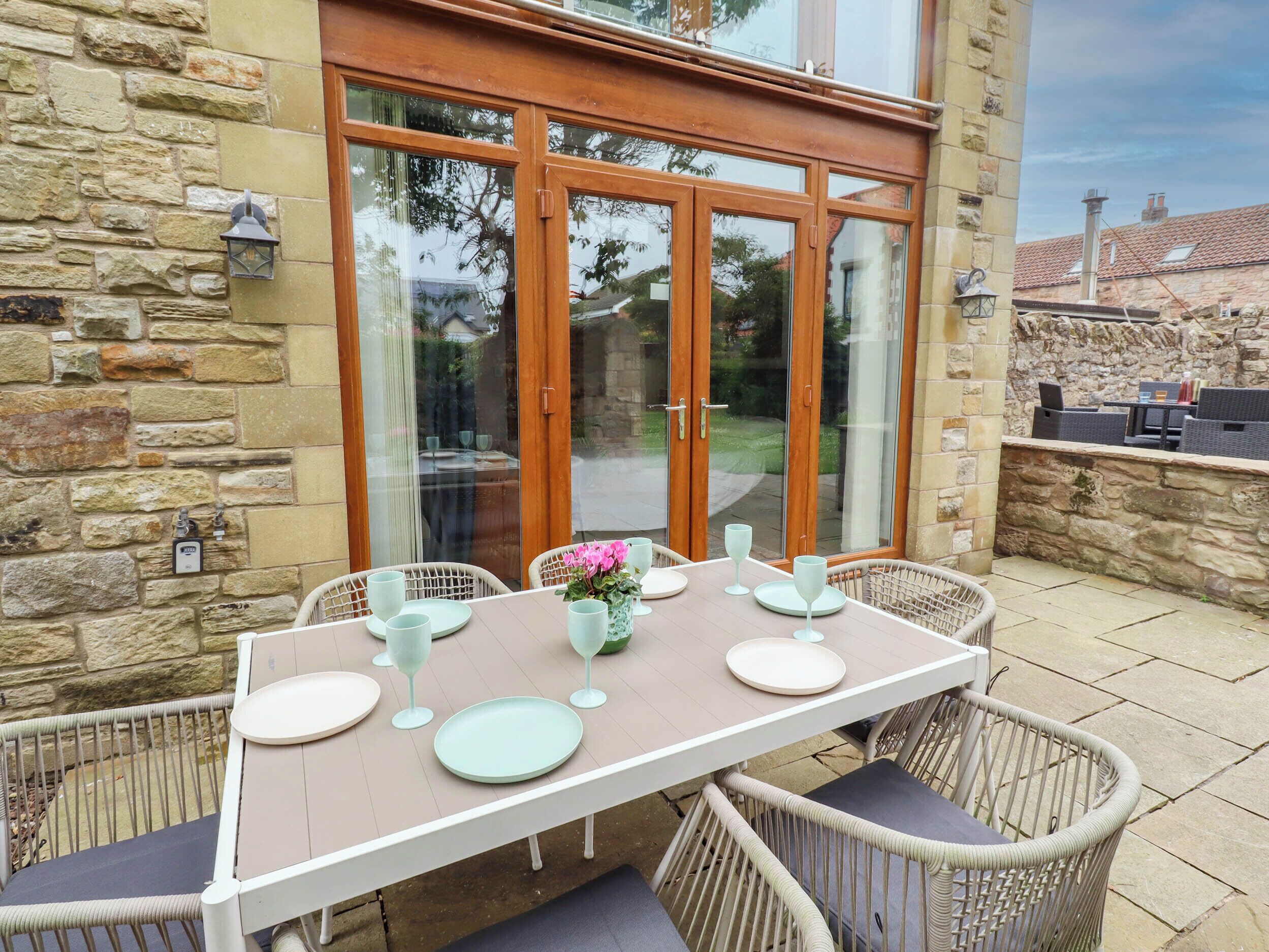Eine Terrasse mit Tisch für vier Personen, Korbstühle und einer Steinmauer.