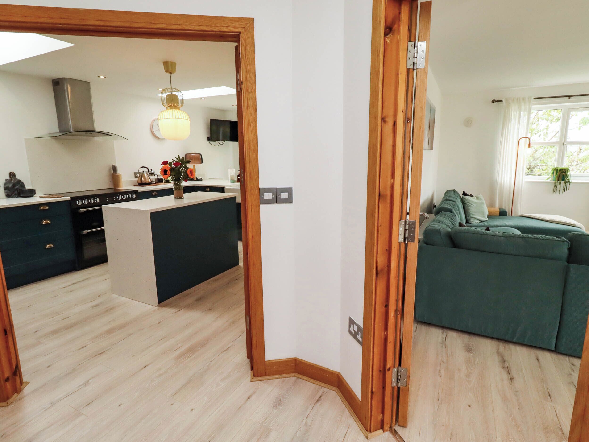 A modern kitchen with a central island, a dining area with a sofa, and a wooden-framed doorway.