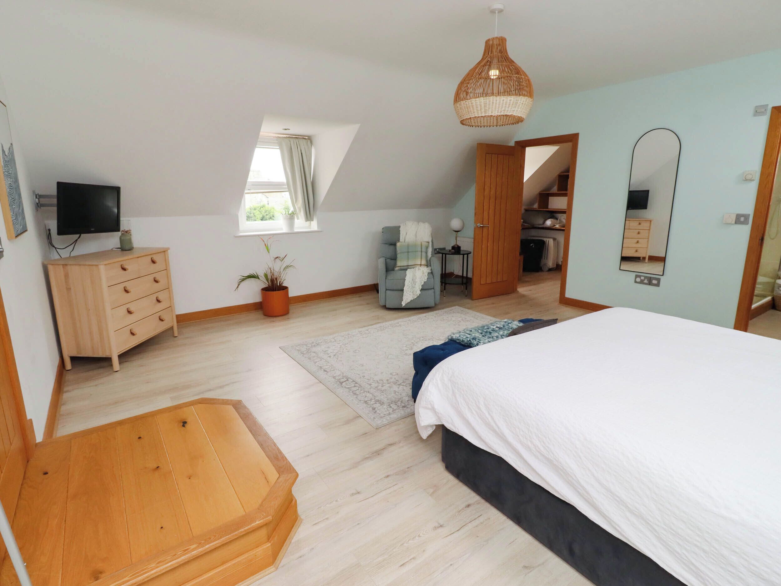 Un dormitorio con cama, cómoda, televisor, ventana, planta, silla y espejo.