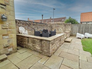 A stone patio with outdoor furniture, a stone wall, and a view of neighboring buildings. - Alma House (Seahouses)