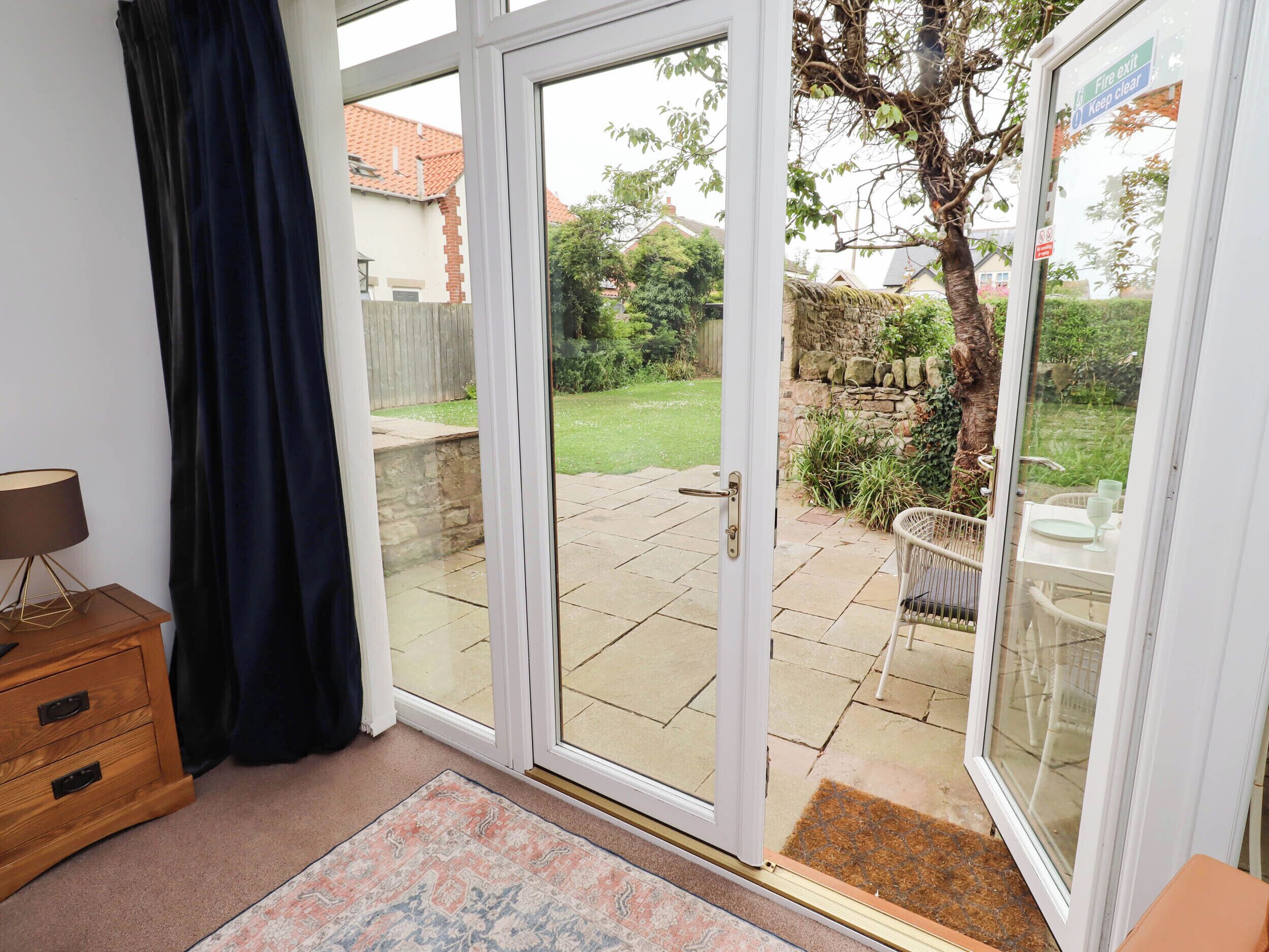 A room with a sliding glass door leading to a patio with a stone floor, a wooden cabinet, and a patterned rug.
