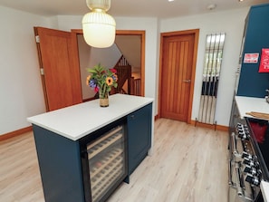 A compact kitchen with a built-in refrigerator, wooden cabinets, and a small island with a vase of flowers. - Alma House (Seahouses)