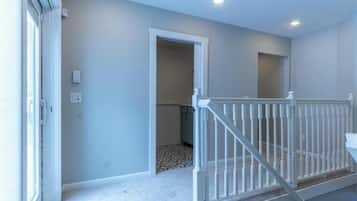 A hallway with a white railing, a door leading to a room, and a light switch on the wall.