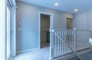 A hallway with a white railing, a door leading to a room, and a light switch on the wall.