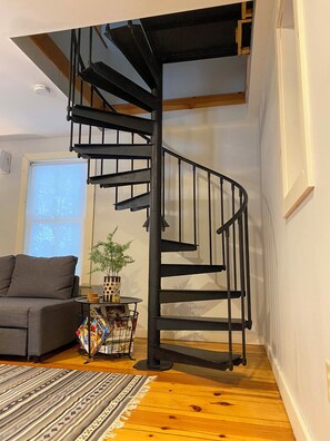 A modern interior with a spiral staircase, a gray sofa, a small table with a plant, and a patterned rug.