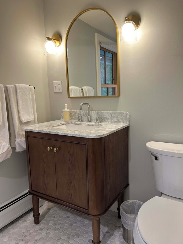 A bathroom with a wooden vanity, a white toilet, and a mirror with wall sconces.