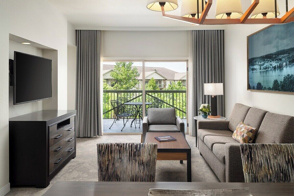 A modern living room with a flat-screen TV, a sofa, a coffee table, and a balcony with outdoor furniture.