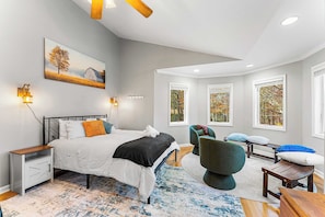 A bedroom with a bed, bedside tables, a chair, a bench, and a painting on the wall.
