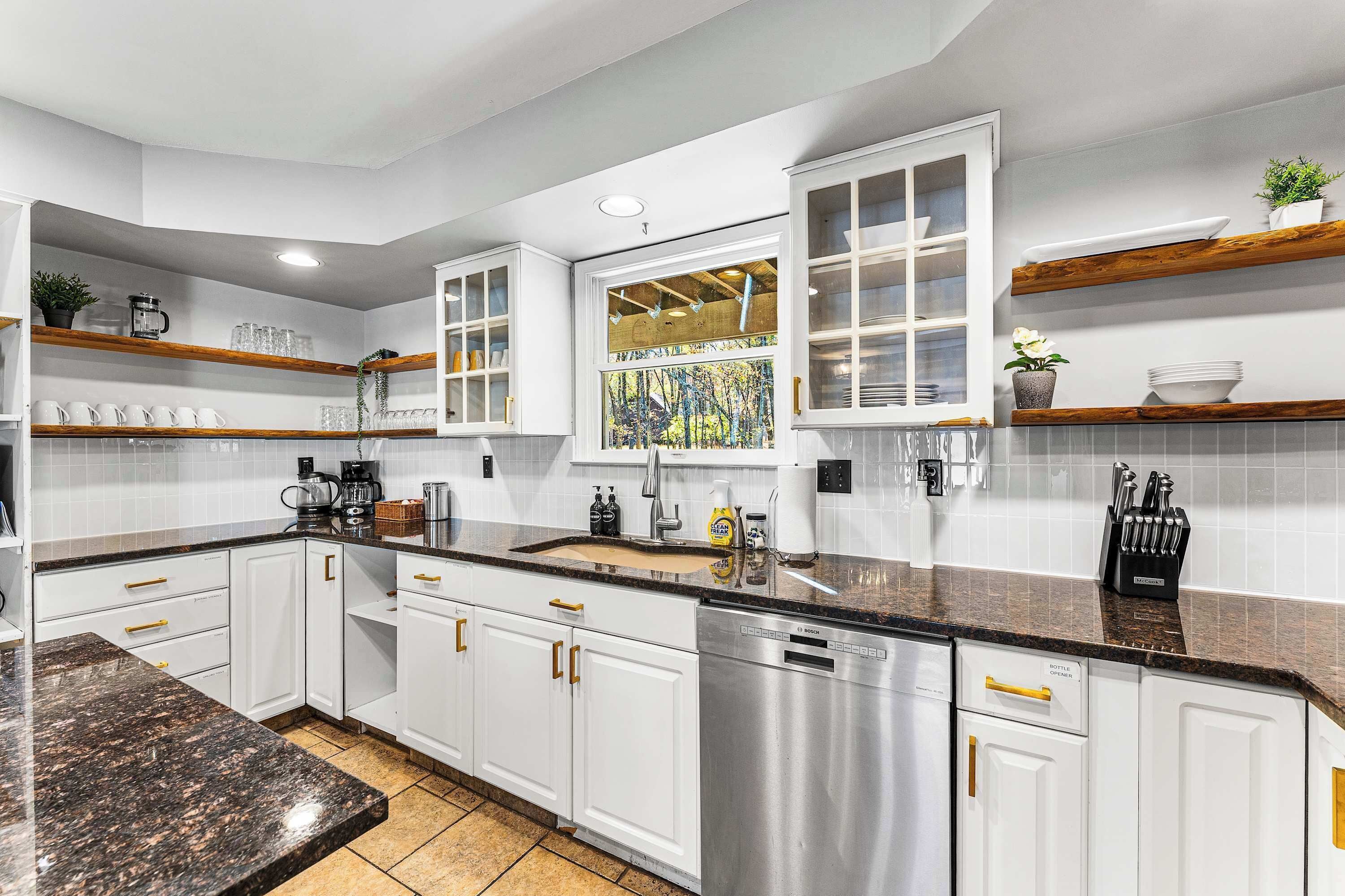 A modern kitchen with white cabinetry, a granite countertop, and a window with a view of a garden.