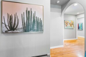 A hallway with a cactus painting, wooden flooring, and two abstract paintings on the wall.