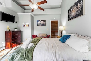 A bedroom with a bed, a ceiling fan, a TV, a dresser, a painting, and a door leading to another room. - 6BR, Sleeps 16, Game Room, Hot Tub, Resort Access (Albrightsville)