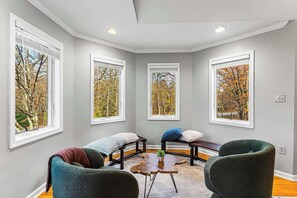 A room with a corner seating area, large windows with a view of trees, and a ceiling with recessed lighting.