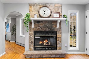 A stone fireplace with a clock above it, a mantel shelf with a framed picture, and a window with a view of trees. - 6BR, Sleeps 16, Game Room, Hot Tub, Resort Access (Albrightsville)