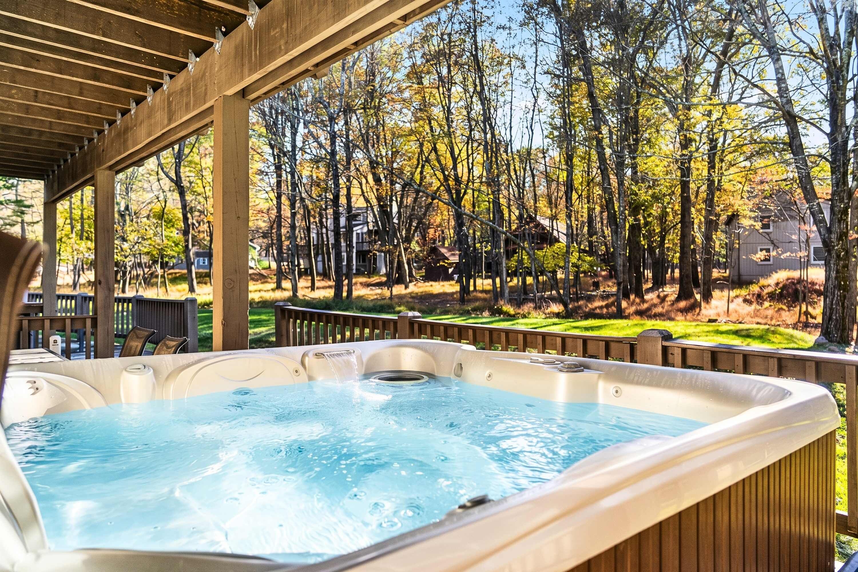 Een hottub onder een houten pergola met uitzicht op een woonwijk en bomen.
