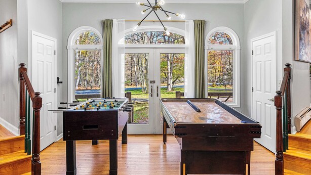 Um quarto com mesa de bilhar, mesa de futebol de mesa e uma grande janela em arco com vista para árvores.