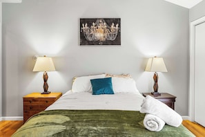 A hotel room with a bed, two bedside tables, a chandelier, and a painting on the wall.