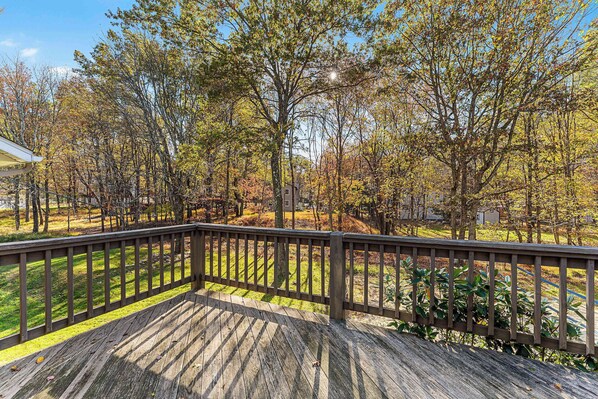 A wooden deck with a railing, surrounded by trees with autumn foliage.