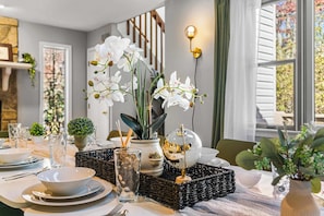 A dining table set with white plates, bowls, and cutlery, accompanied by a glass vase with white flowers, a glass vase with black pebbles, and a decorative globe. - 6BR, Sleeps 16, Game Room, Hot Tub, Resort Access (Albrightsville)