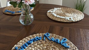 Une table en bois avec des sets de table en fibres tressées, un vase avec des fleurs et, au fond, un appareil électroménager blanc.