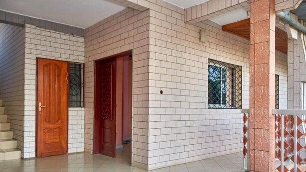 Un bâtiment doté d’un sol carrelé, d’une porte en bois et d’une fenêtre protégée par une grille métallique.