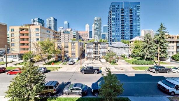 Paisagem urbana com edifícios altos modernos, um estacionamento com carros e um céu azul claro.